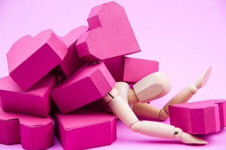 Wooden dummy was crushed by a pile of paper box red heart shape on pink background with copy space for your text.Concept Valentine's Day, Day of loveの写真素材