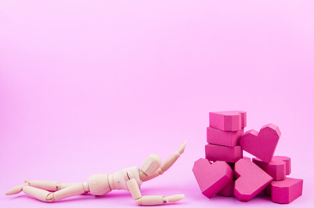 Wooden dummy was crawling to a pile of paper box red heart shape on pink background with copy space for your text.Concept Valentine's Day, Day of loveの写真素材