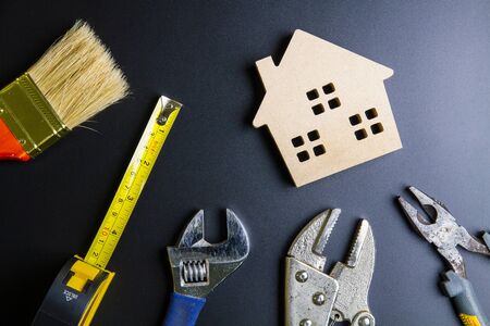 Wooden house toy and construction tools on black background with copy space.Real estate concept, New house concept, Finance loan business concept, Repair maintenance conceptの写真素材