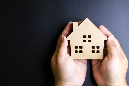 Man's hand holding wooden house toy on black background with copy space.Real estate concept, New house concept, Finance loan business conceptの写真素材