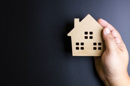 Man's hand holding wooden house toy on black background with copy space.Real estate concept, New house concept, Finance loan business conceptの写真素材