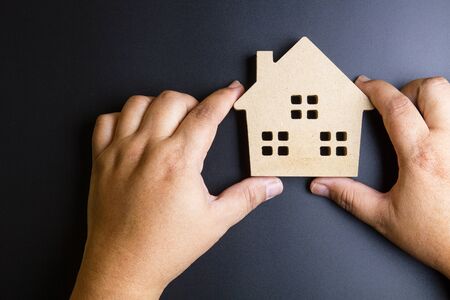 Man's hand holding wooden house toy on black background with copy space.Real estate concept, New house concept, Finance loan business conceptの写真素材