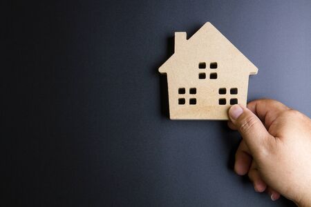 Man's hand holding wooden house toy on black background with copy space.Real estate concept, New house concept, Finance loan business conceptの写真素材
