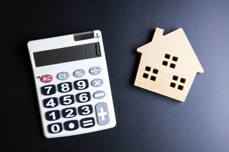 Wooden house toy and calculator on black background with copy space.Real estate concept, New house concept, Finance loan business conceptの写真素材