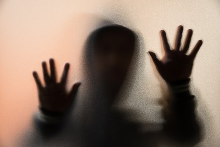Shadow blur of horror man in jacket with hood.Hands on the glass.Dangerous man behind the frosted glass.Mystery man.Halloween background.Blur pictureの写真素材