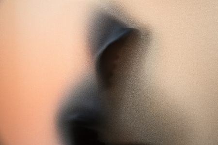 Shadow blur of horror man in jacket with hood.Dangerous man behind the frosted glass.Mystery man.Halloween background.Blur pictureの写真素材