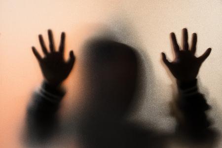 Shadow blur of horror man in jacket with hood.Hands on the glass.Dangerous man behind the frosted glass.Mystery man.Halloween background.Blur pictureの写真素材