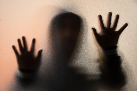 Shadow blur of horror man in jacket with hood.Hands on the glass.Dangerous man behind the frosted glass.Mystery man.Halloween background.Blur pictureの写真素材