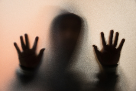 Shadow blur of horror man in jacket with hood.Hands on the glass.Dangerous man behind the frosted glass.Mystery man.Halloween background.Blur pictureの写真素材