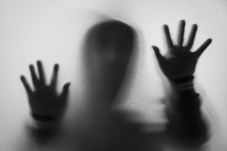 Shadow blur of horror man in jacket with hood.Hands on the glass.Dangerous man behind the frosted glass.Mystery man.Halloween background.Black and white picture.Blur pictureの写真素材
