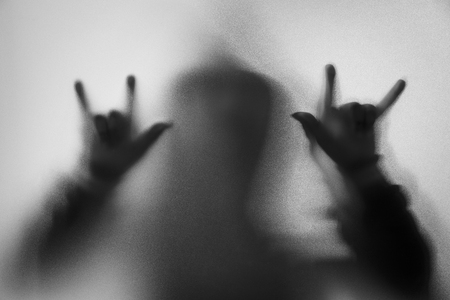 Shadow blur of horror man in jacket with hood.Hands do as a symbol love on the glass.Dangerous man behind the frosted glass.Mystery man.Halloween background.Black and white picture.Blur pictureの写真素材