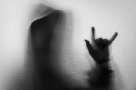 Shadow blur of horror man in jacket with hood.Hands do as a symbol love on the glass.Dangerous man behind the frosted glass.Mystery man.Halloween background.Black and white picture.Blur pictureの写真素材