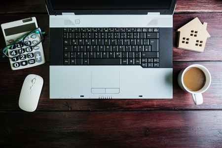 Top view of office stuff with laptop wireless mouse calculator coffee cup and wooden house toy on wooden table.Concept workplace.Real estate concept, New house concept, Finance loan business conceptの写真素材