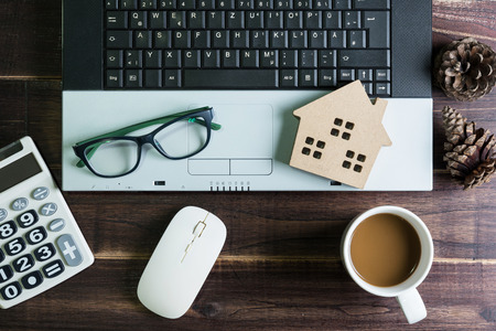Top view of office stuff with laptop wireless mouse calculator coffee cup and wooden house toy on wooden table.Concept workplace.Real estate concept, New house concept, Finance loan business conceptの写真素材