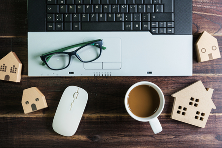 Top view of office stuff with laptop wireless mouse coffee cup and wooden house toy on wooden table.Concept workplace.Real estate concept, New house concept, Finance loan business conceptの写真素材