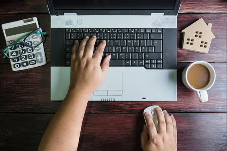 Top view of office stuff hand on wireless mouse with laptop calculator wooden house toy and coffee cup on wooden table.Concept workplace.Real estate concept, New house concept, Finance loan business conceptの写真素材