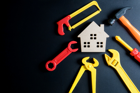 Wooden house toy and construction tools toy on black background with copy space.Home Repair concept, Repair maintenance concept, Renovation concept.の写真素材
