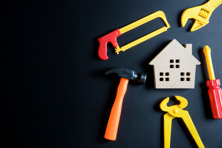 Wooden house toy and construction tools toy on black background with copy space.Home Repair concept, Repair maintenance concept, Renovation concept.の写真素材