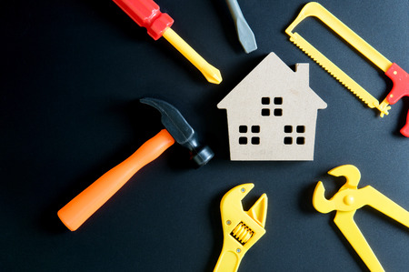 Wooden house toy and construction tools toy on black background with copy space.Home Repair concept, Repair maintenance concept, Renovation concept.の写真素材