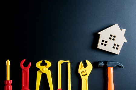 Wooden house toy and construction tools toy on black background with copy space.Home Repair concept, Repair maintenance concept, Renovation concept.の写真素材