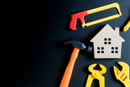 Wooden house toy and construction tools toy on black background with copy space.Home Repair concept, Repair maintenance concept, Renovation concept.の写真素材