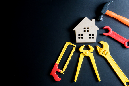 Wooden house toy and construction tools toy on black background with copy space.Home Repair concept, Repair maintenance concept, Renovation concept.の写真素材