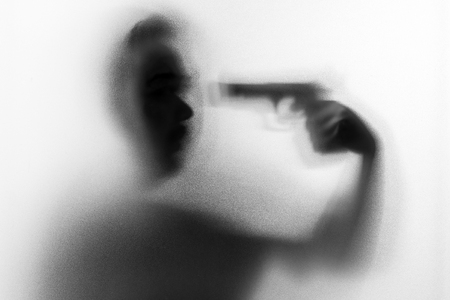 Shadow of horror man killer with a gun in his hand.Dangerous man behind the frosted glass.Mystery man.Halloween background.Black and white picture.Blur pictureの写真素材