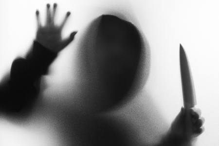 Shadow blur of horror man in jacket with hood knife in his hand.Dangerous man behind the frosted glass.Mystery man.Halloween background.Black and white picture.Blur pictureの写真素材