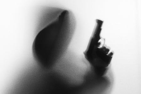 Shadow blur of horror man in jacket with hood gun in his hand.Dangerous man behind the frosted glass.Mystery man.Halloween background.Black and white picture.Blur pictureの写真素材