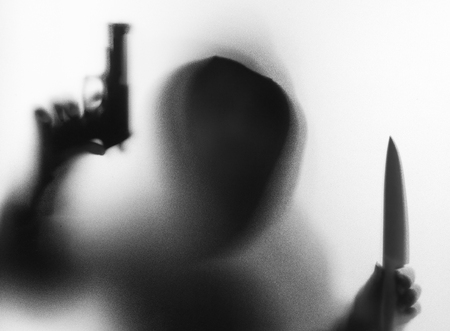 Shadow blur of horror man in jacket with hood knife and gun in his hand.Dangerous man behind the frosted glass.Mystery man.Halloween background.Black and white picture.Blur pictureの写真素材