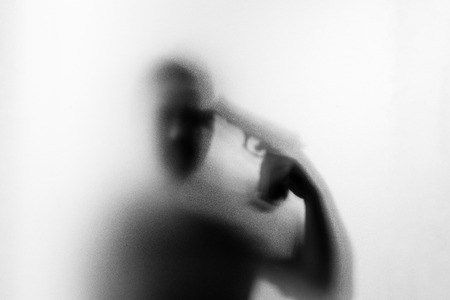 Shadow of horror man killer with a gun in his hand.Dangerous man behind the frosted glass.Mystery man.Halloween background.Black and white picture.Blur pictureの写真素材