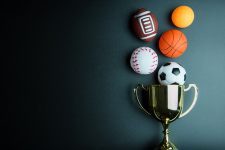Golden trophy, Football toy, Baseball toy, Ping pong ball, Basketball toy and Rugby toy isolated on black background with copy space.Concept winner of the sportの写真素材