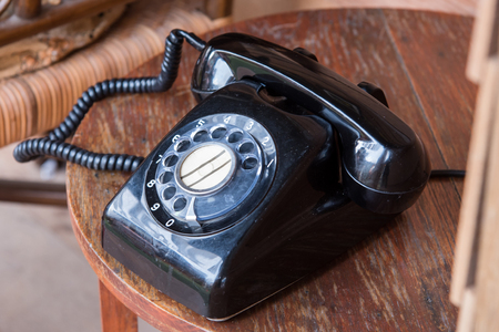 Black antique vintage analog telephone dialing or scrolling phone on wooden tableの写真素材