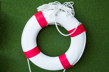 White Red lifebuoy with rope on green artificial grass wall