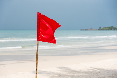 Warning sign of a red flag at a beautiful beach with a blue sky at Prao Beach in Trat, Thailandの写真素材