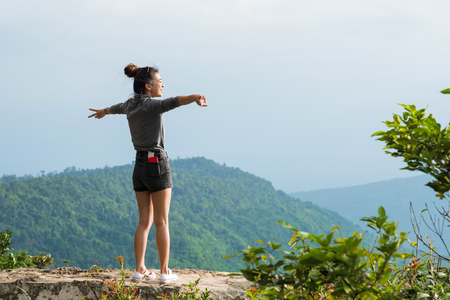 Chaiyaphum, Thailand - July, 01, 2017 : Freedom traveler woman standing with raised arms and enjoying a beautiful nature on a cliff edge on the top of mountain with gorgeous view at Chaiyaphum, Thailandのeditorial素材
