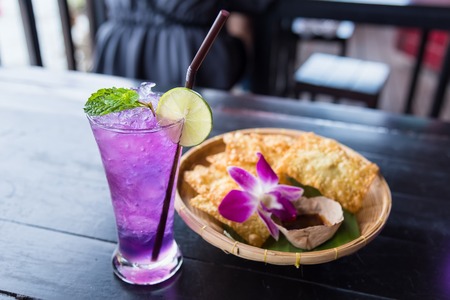 Butterfly pea iced soft drinks with lemon slice and peppermint on top and on the wooden table at the riverside restaurant.Thailandの写真素材