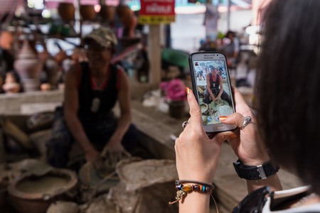 Nonthaburi, Thailand - December, 17, 2017 : Unidentified name Tourists are taking pictures traditional potter man making shaping a jar on the spinning by clay with a smartphone at Koh Kret Nonthaburi, Thailand.のeditorial素材