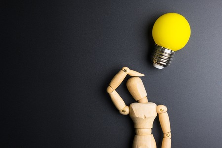 Wooden dummy toy and light bulb on black background with copy spaceの写真素材