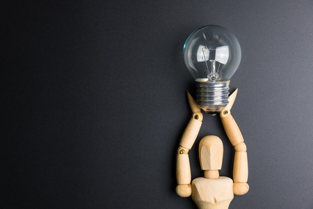 Wooden dummy toy and light bulb on black background with copy spaceの写真素材