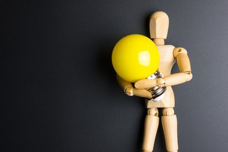 Wooden dummy toy and light bulb on black background with copy spaceの写真素材