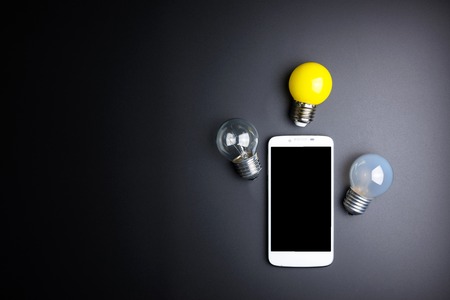 Smartphone and light bulb on black background with copy spaceの写真素材