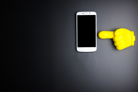 Smartphone and yellow plastic hand pointing on black background with copy spaceの写真素材