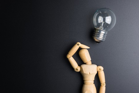 Wooden dummy toy and light bulb on black background with copy spaceの写真素材