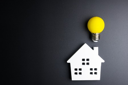 White house toy and light bulb on black background with copy space.Real estate concept, New house concept, Finance loan business concept, Repair maintenance conceptの写真素材