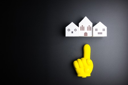 White house toy and yellow plastic hand pointing on black background with copy space.Real estate concept, New house concept, Finance loan business concept, Repair maintenance conceptの写真素材