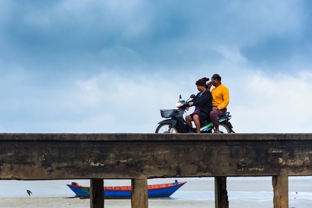 Chanthaburi, Thailand - April, 28, 2018 : Fishing man ride old motorcycle on the chaolao harbor bridge in the morning over cloudy sky at Chanthaburi, Thailandのeditorial素材