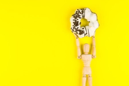 Wooden dummy holding Donut made at home on yellow background.High energy foods to work.Foods with...