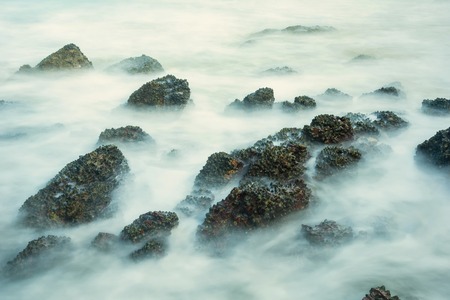 Long exposure seascape with foamy waves splashing against a rocky shore of thailand in the morning timeの写真素材