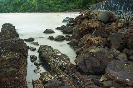 Long exposure seascape with foamy waves splashing against a rocky shore of thailand in the morning timeの写真素材